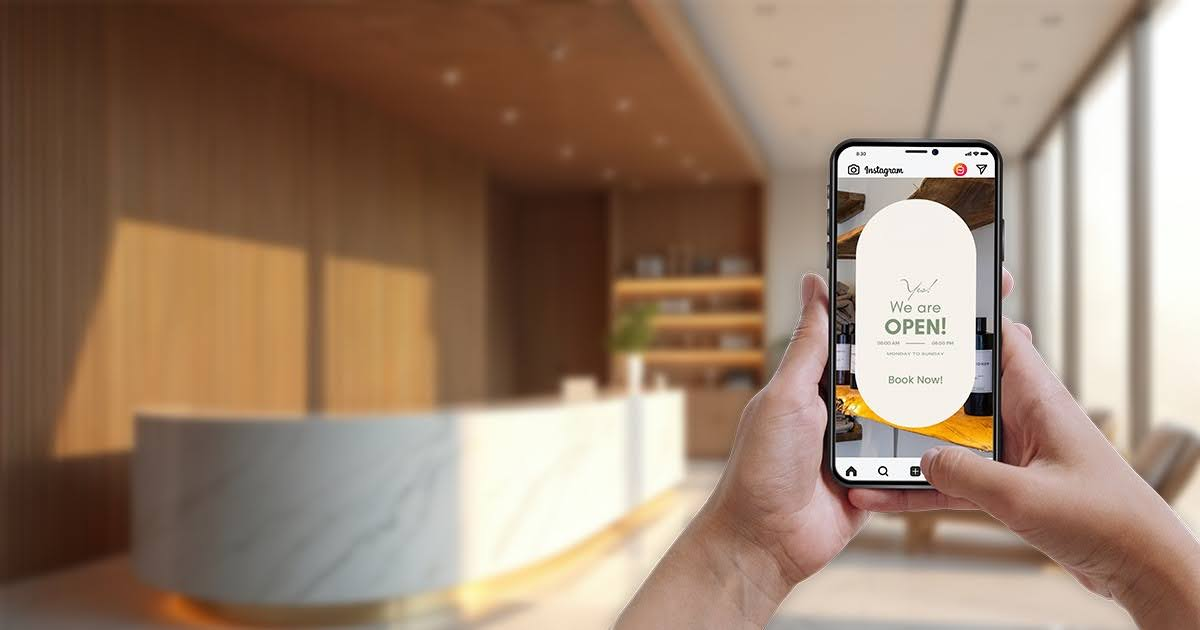 Person holding a smartphone displaying an Instagram Story with a "We are OPEN! Book Now!" message, set against a blurred modern reception or salon interior